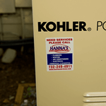 White rectangle weatherproof vinyl label with red text and blue graphic on outdoor air conditioner.