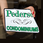 White static cling window decal with green Pederson Condominiums text being applied on glass window.