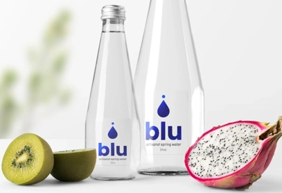 Two glass water bottles with sleek, transparent retail labels featuring the brand name "blu" and a water droplet logo, set against a fresh fruit backdrop. Ideal for premium beverage branding and retail packaging.